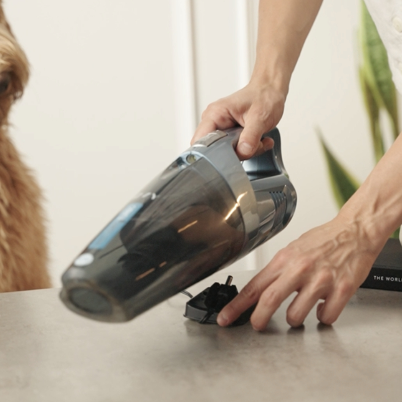 Απεικονίζεται το ηλεκτρικό σκουπάκι χειρός να τοποθετείται στην βάση φόρτισης του.